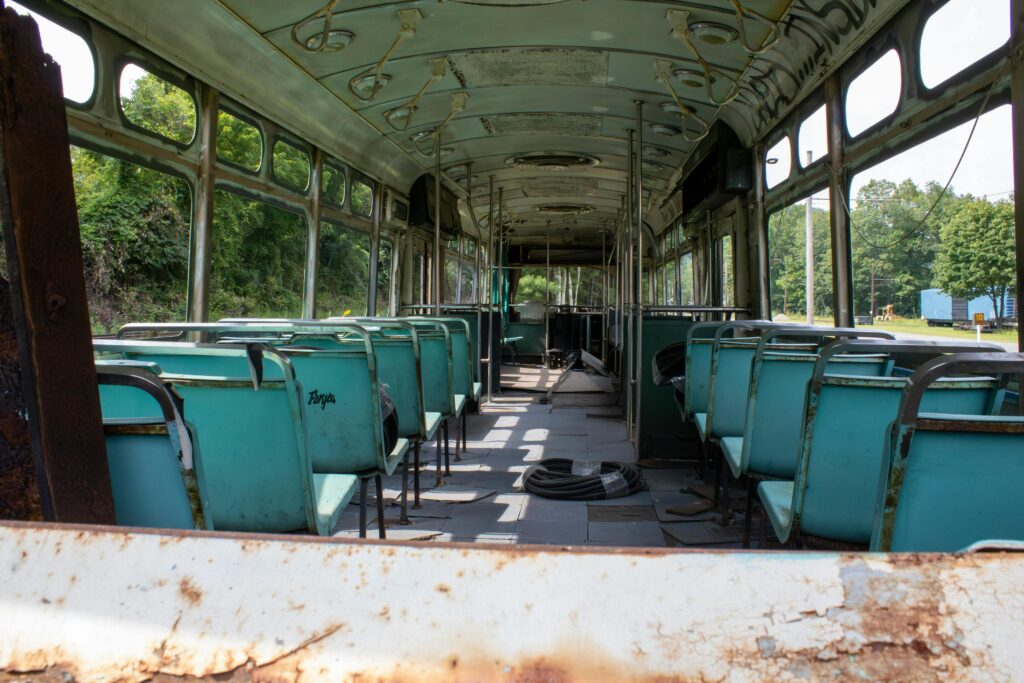 Explore the inside of an abandoned, rusty bus with sunlight streaming through, highlighting teal seats.